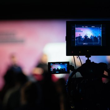 A camera filming people talking on stage