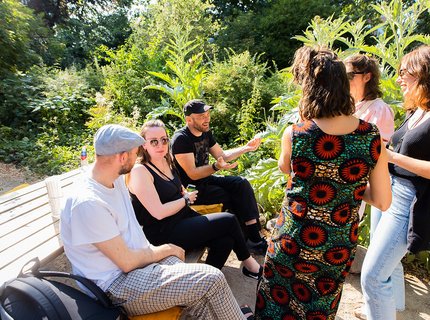 A group of people sitting and standing around a bench.