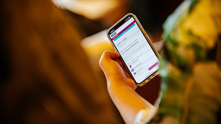 Eine Nahaufnahme einer Hand, die ein Telefon hält, auf dem der Zeitplan des Mozilla Festivals zu sehen ist.