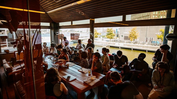 Eine Gruppe von Menschen saß um einen Tisch in einer MozFest House-Session, mit einem Fenster im Hintergrund mit Blick auf einen Fluss.