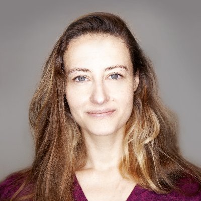 A person with long brown hair wearing a red shirt smiling at the camera
