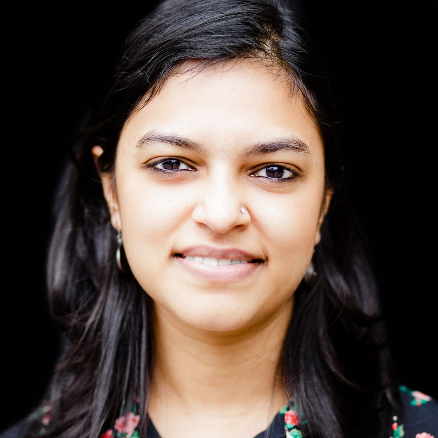 A person with dark long hair against a black background smiling at the camera