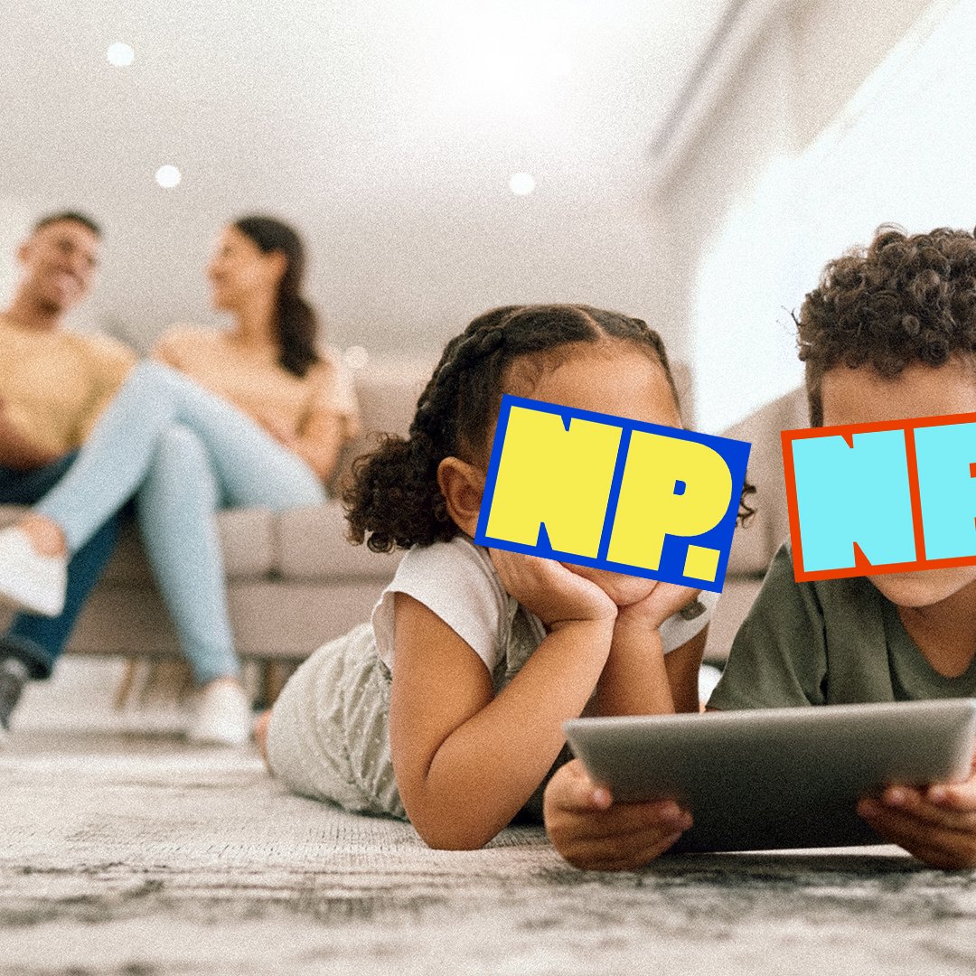 Two kids playing on a tablet with parents in the background.