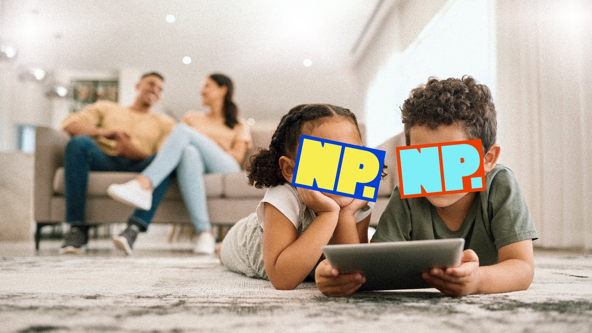 Two kids playing on a tablet with parents in the background.