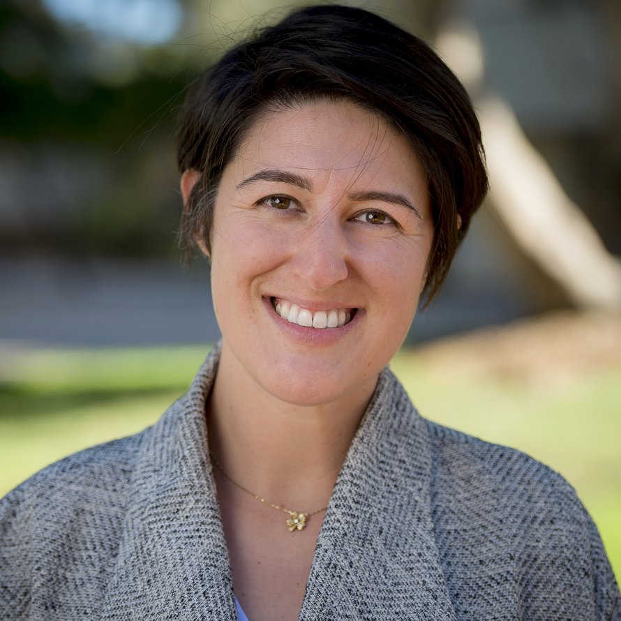A person with short dark hair wearing a gray sweater smiling at the camera