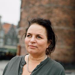 A person with medium length dark hair wearing a green button-up shirt looking off into the distance