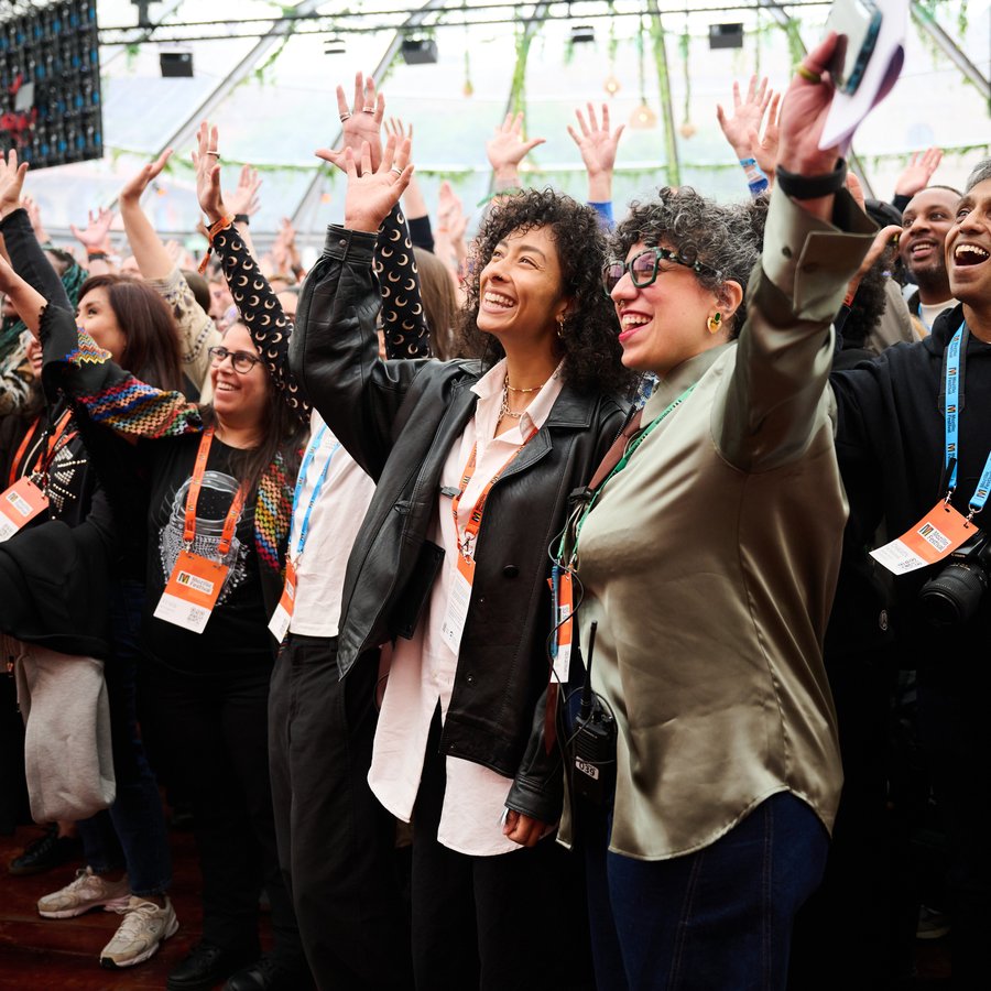 People smile and raise their hands in an event space auditorium with a clear roof