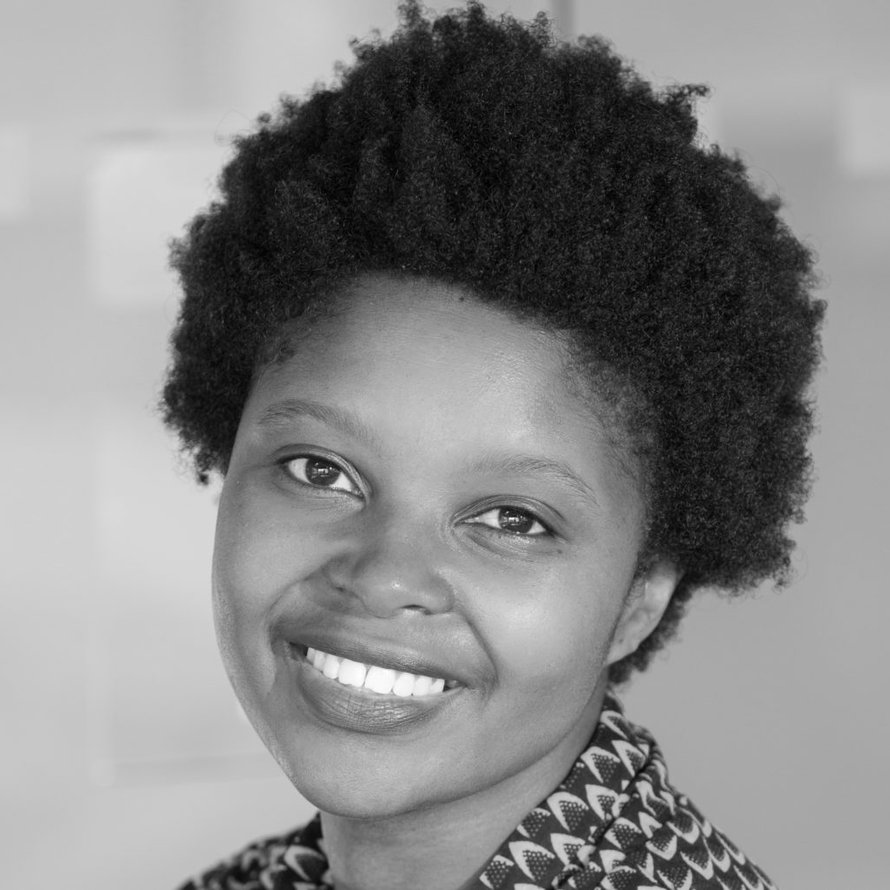 A black and white photo of a person with short dark hair wearing a patterned shirt smiling at the camera