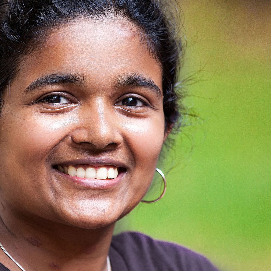 A person with dark short hair wearing gold hoop earrings smiling at the camera