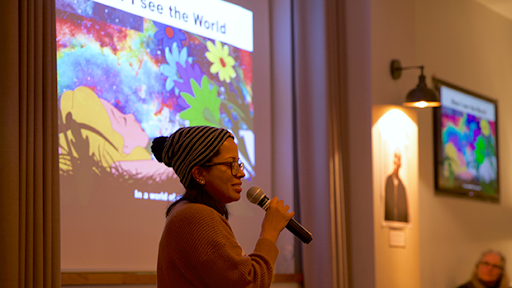 Facilitator speaking into a microphone with projector screen in the background.