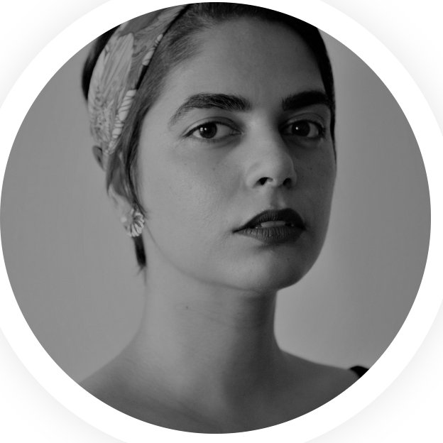 A headshot of a person with their hair pulled up into a cloth wrap looking at the camera
