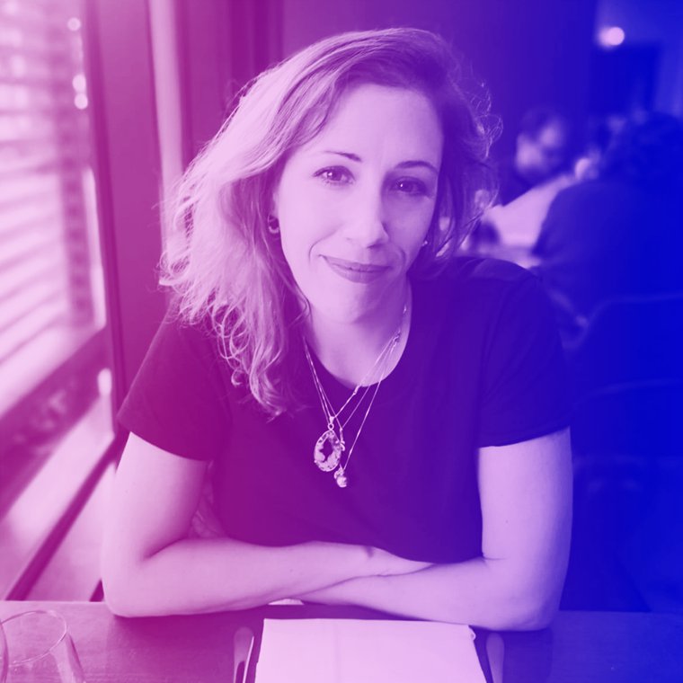 Person smiling at the camera with arms folded leaning against a table. Purple and pink overlay on photo.