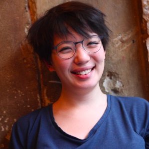 Person smiling at the camera with short black hair, dark rimmed glasses and a blue shirt