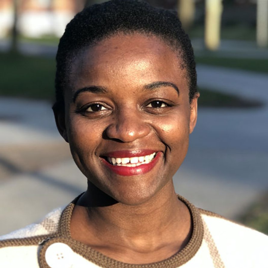 Person with short dark hair and a white sweater with olive green accents smiling at the camera
