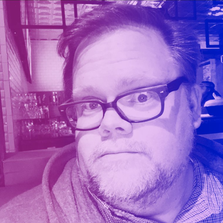 A pale-skinned, fat man with short hair, a short beard, and dark rimmed glasses wearing a plaid shirt under a zip-up hoodie looks at the camera. There is a pink-to-purple gradient over the images, as well.