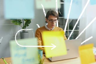 Man with glasses looking at a computer in an office with white hand drawn lines emanating from behind him and an arrow pointing to the laptop
