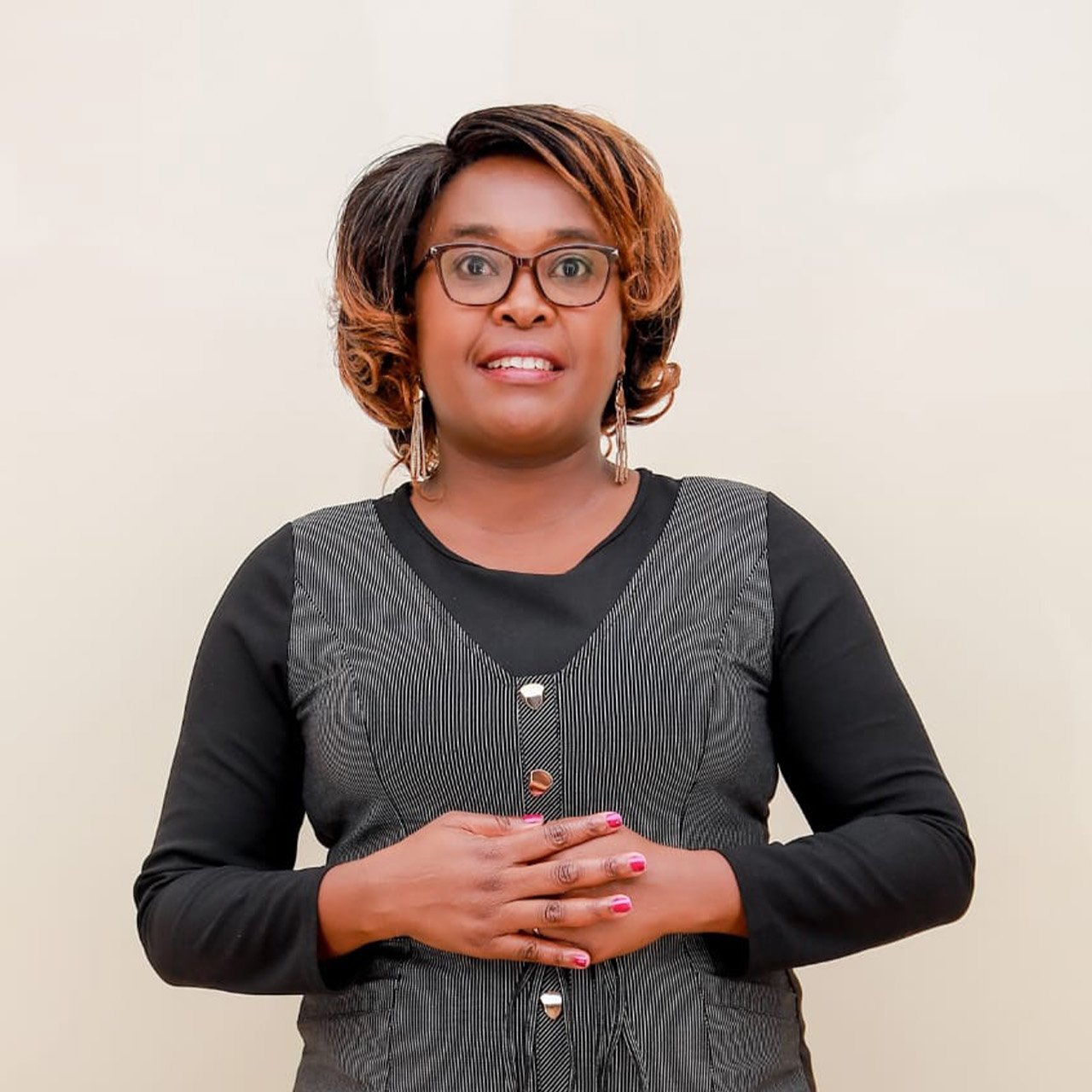 A person standing in front of a white wall with hands clasped